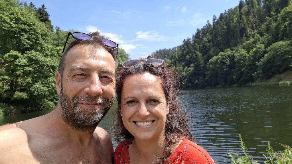 Zufriedenes Paar lächelt am See – Erfolgsgeschichte mit Ackermann Gesund & Vital Nahrungsergänzung für mehr Lebensfreude und Wohlbefinden.