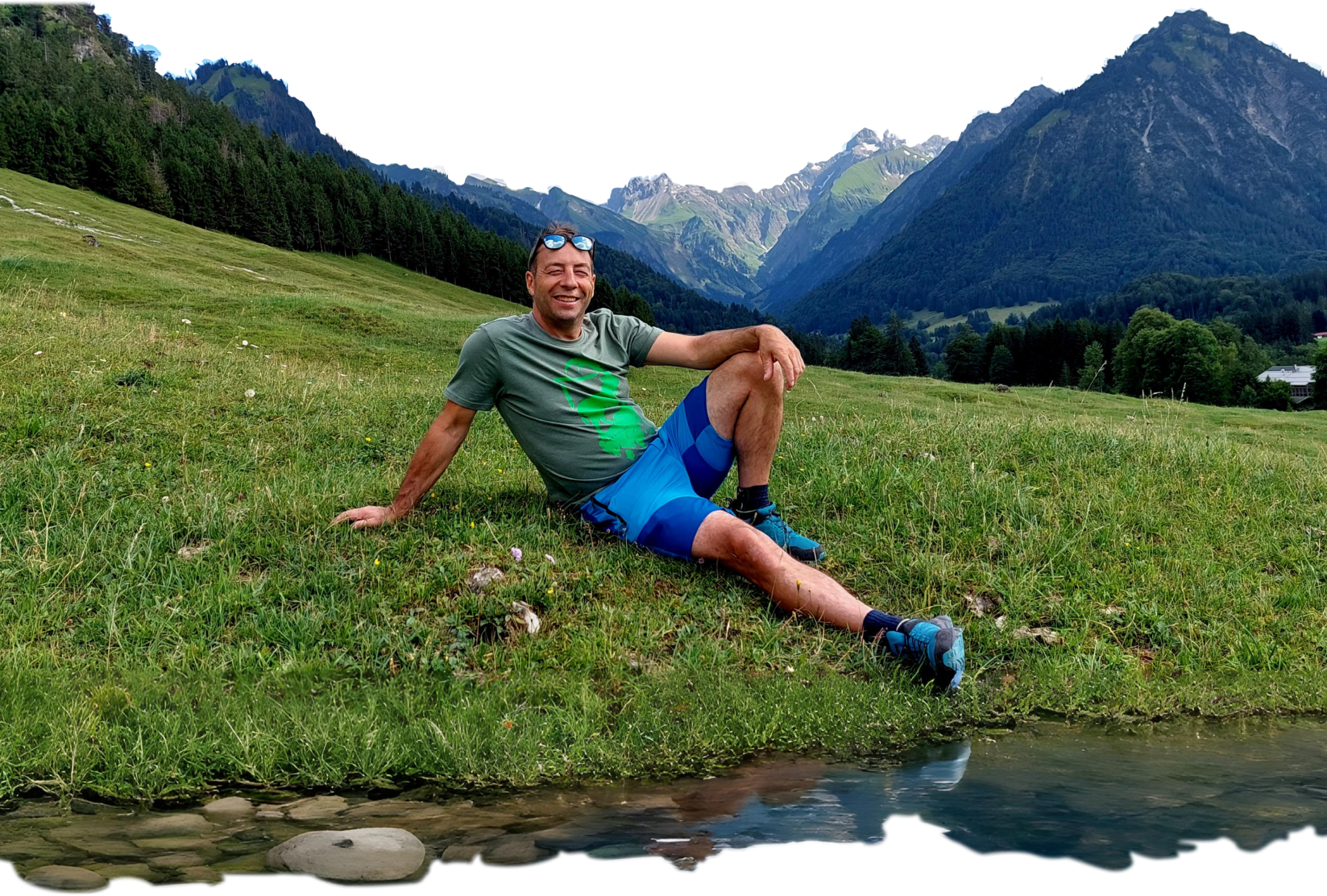 Mann sitzt entspannt in den Bergen und lächelt – Symbol für Vitalität, Energie und erfolgreiche körperliche Veränderung.